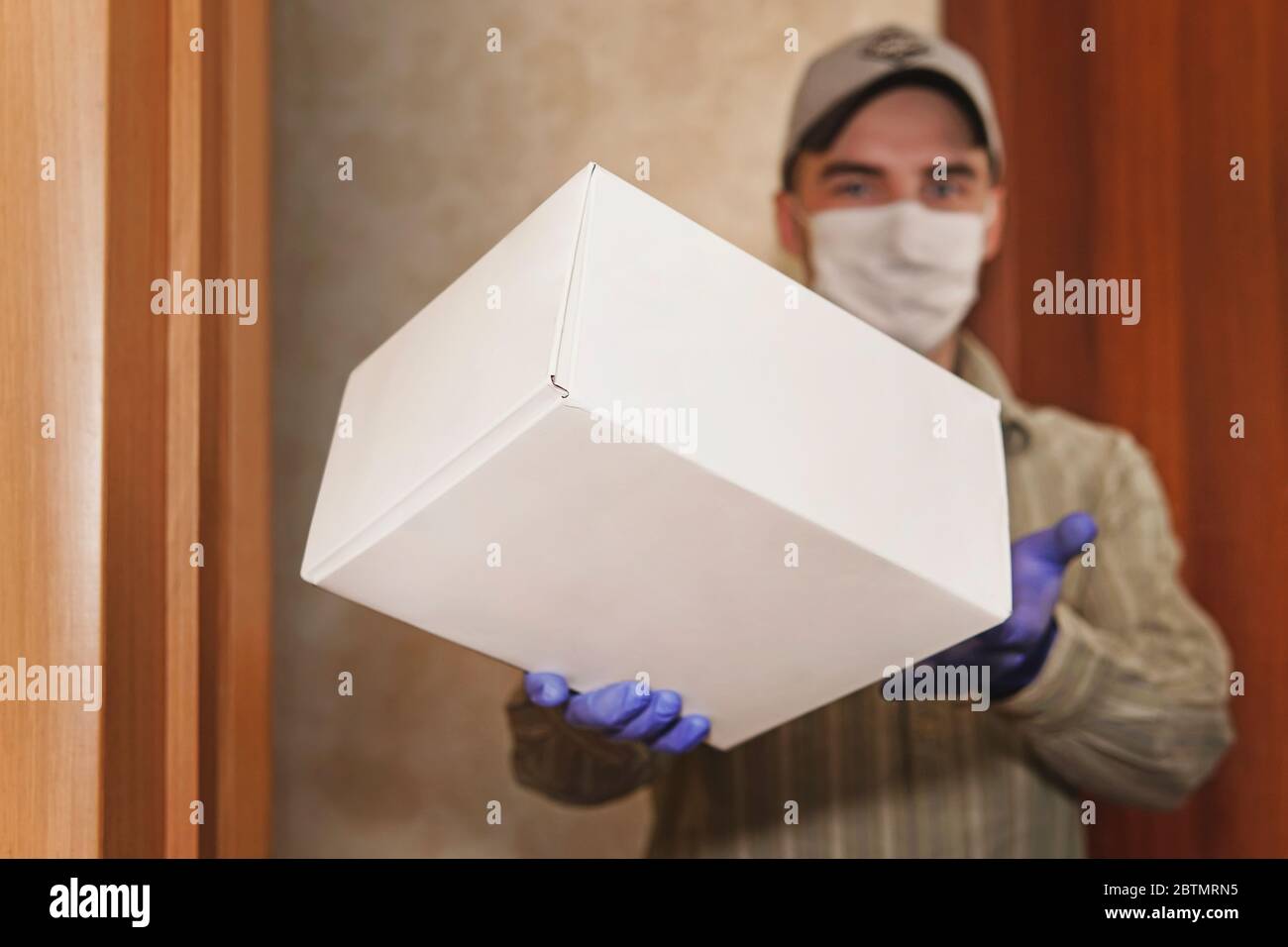 Nach Hause liefern, Online-Bestellung. Mann in einer medizinischen Maske und Gummihandschuhe mit weißen Box, ein Paket in den Händen. Lieferung während der Quarantäne der Stockfoto