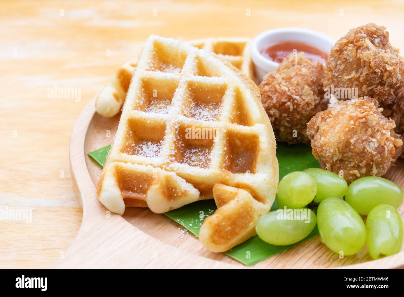 Waffeln mit gebratenem Hühnerball und Traube in Holzschale auf Holztisch. Stockfoto