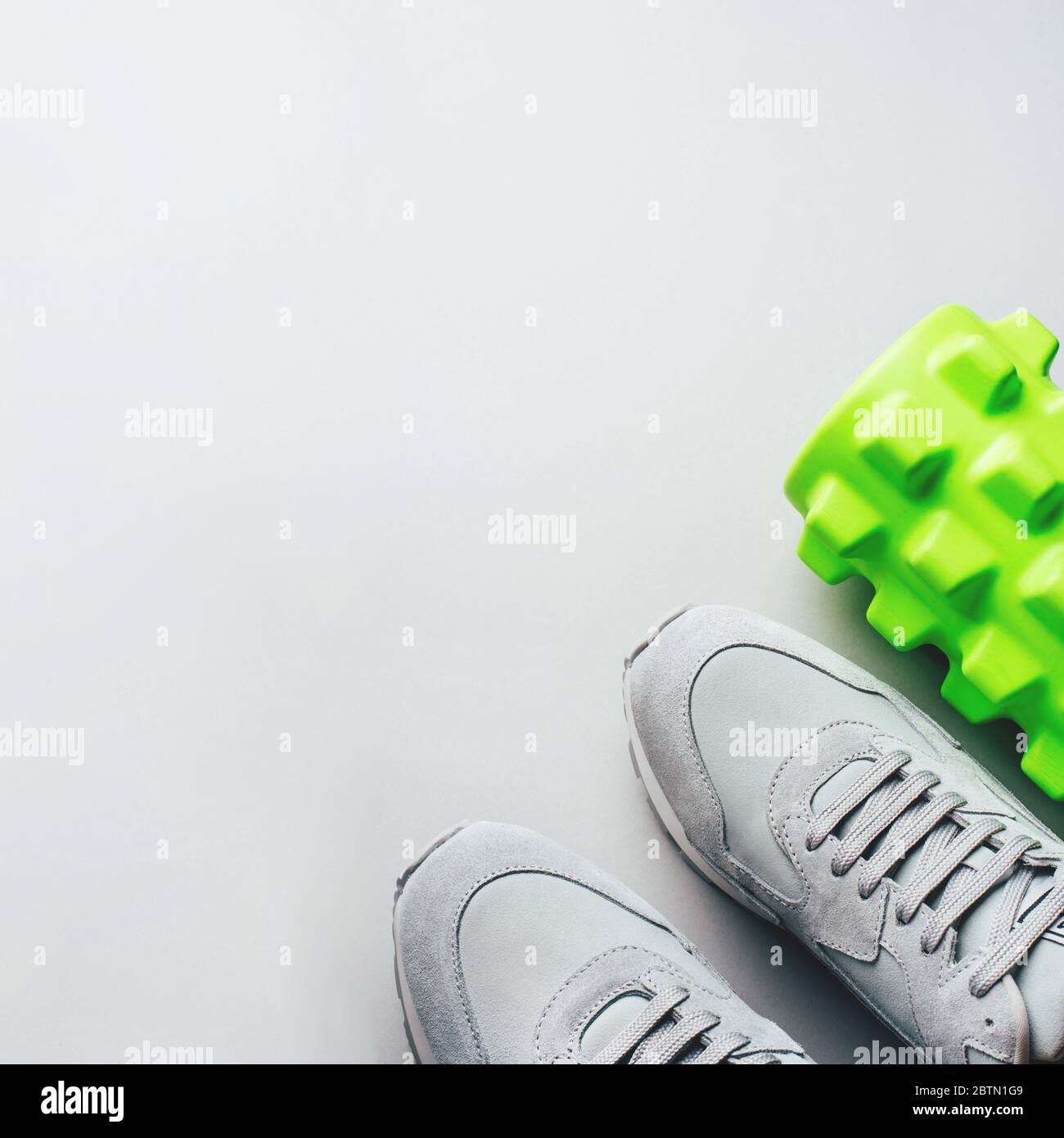 Graue Sneaker und Massageroller auf grauem Hintergrund. Stockfoto