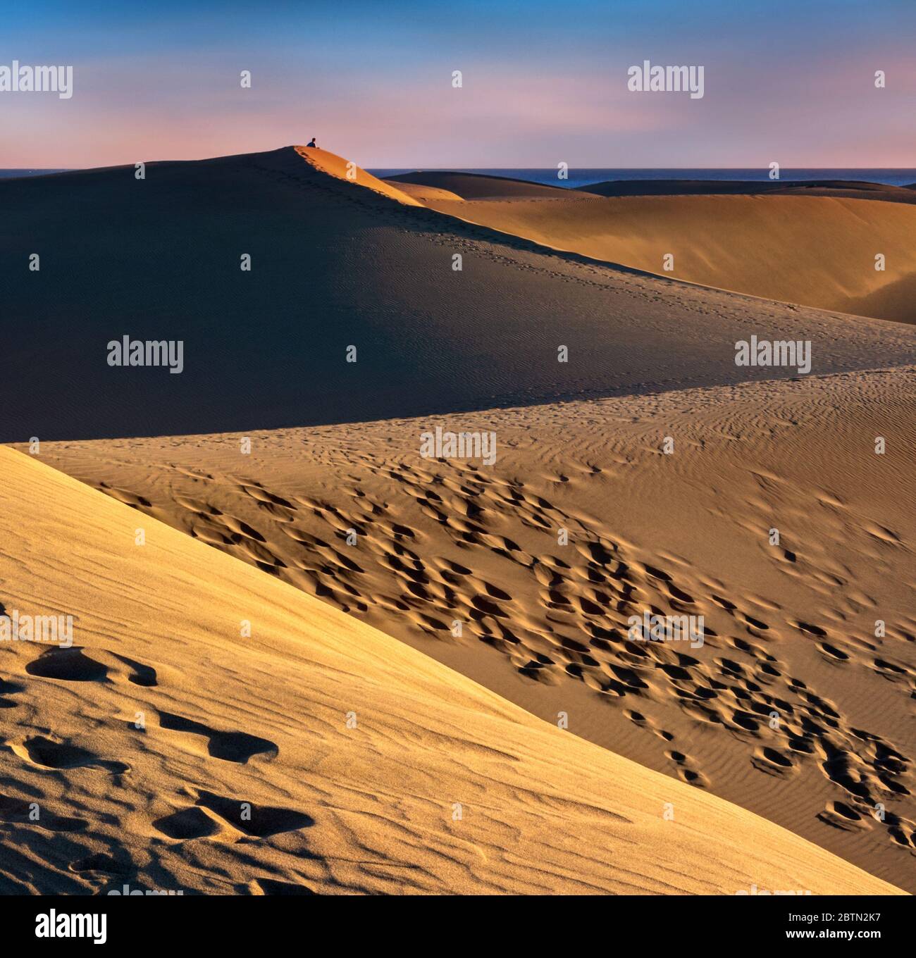 Die herrlichen Dünen von Maspalomas auf Gran Canaria, bei Sonnenuntergang mit einer einsamen Person im Hintergrund, die auf das Meer starrt Stockfoto