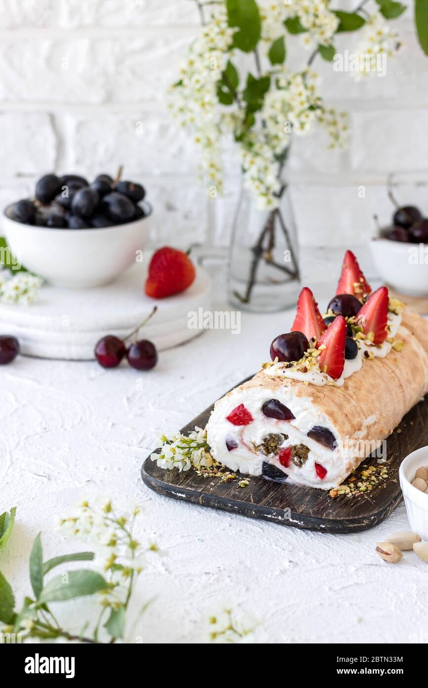 Meringue-Rolle mit frischen Pistazien-Pralinbeeren und Schlagsahne und Quark-Käsecreme. Sommerdessert Stockfoto