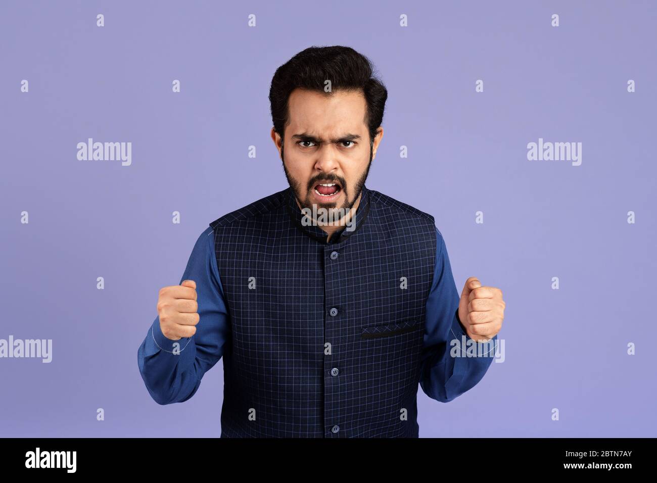 Tausendjähriger Indianer, der seine Fäuste vor Farbergrund in Wut zusammenklammend Stockfoto