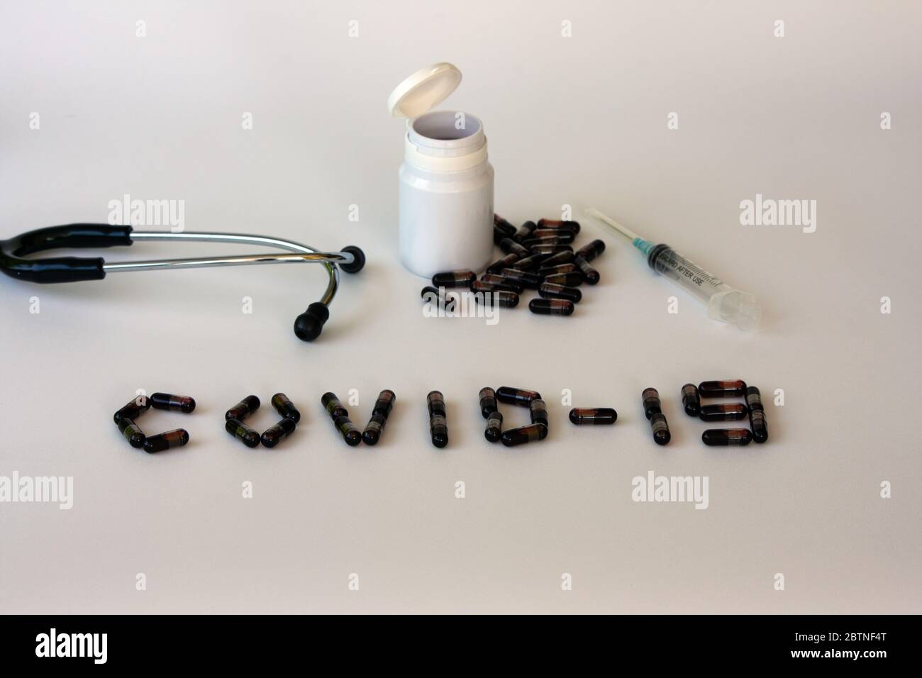 Kapseln, die aus einer weißen Flasche mit einem Stethoskop und einer Spritze von oben heraus verschüttet wurden. Behandlungskonzept für Coronavirus. Stockfoto