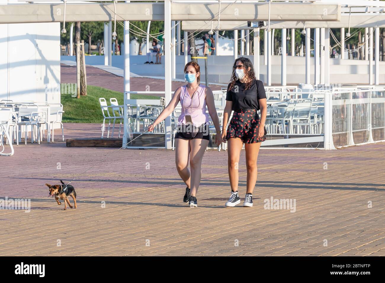 Huelva, Spanien - 23. Mai 2020: Frau, die ihren Hund bei Sonnenuntergang an der Huelva Promenade entlang geht, während des Alarmzustandes eine schützende oder medizinische Gesichtsmaske trägt Stockfoto