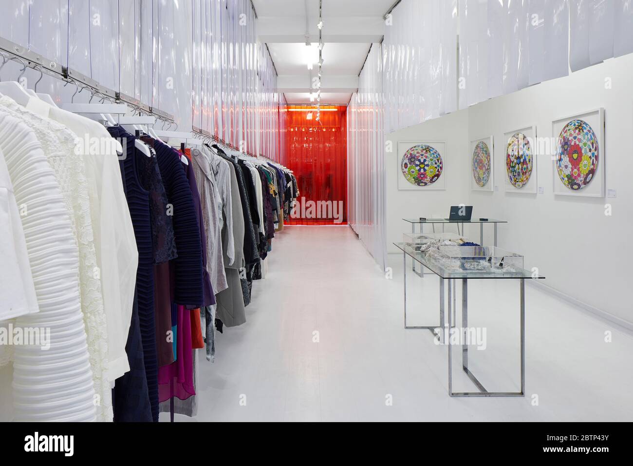 Regale mit japanischer Designer-Kleidung Rote Vinylvorhänge trennen die Umkleidekabinen vom Ladenboden. Butikku, London, Großbritannien. Architekt: Soh Stockfoto