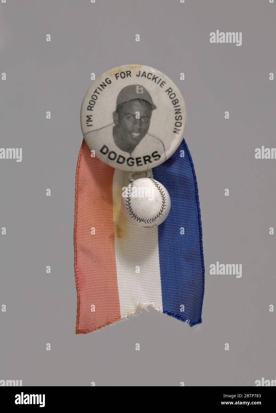 Pinback Knopf von Jackie Robinson mit Baseball Charme und Band. Ein Metallknopf mit einem Bild von Jackie Robinson mit den Worten [Ich BIN FÜR JACKIE ROBINSON GEWURZELT] oben und [DODGERS] unten. An der Unterseite des Stiftes ist ein kleiner Charme in Form eines Baseball angebracht. Stockfoto