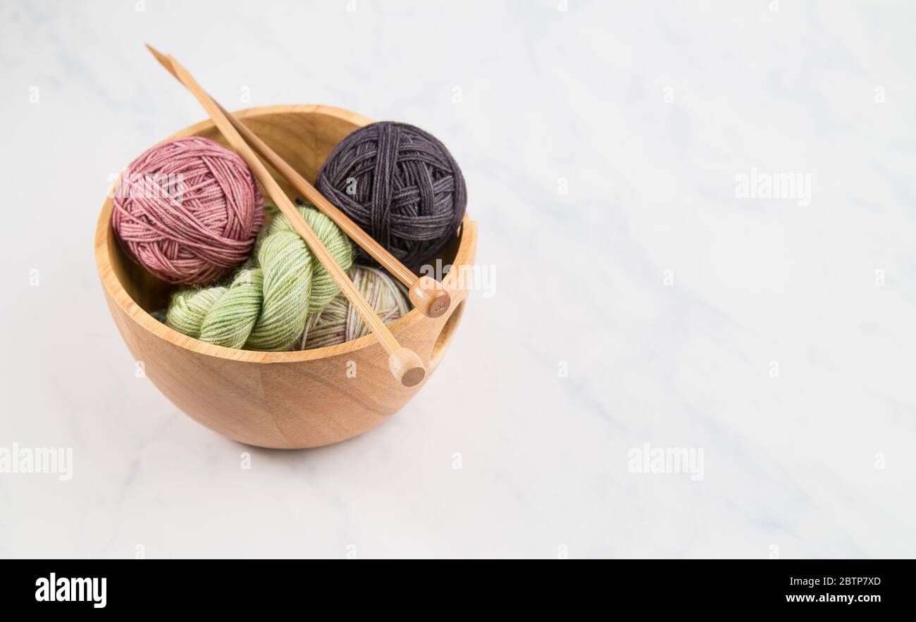 Strickschale voll von bunten Garnkugeln mit Holzstricknadeln auf neutralem Hintergrund Stockfoto