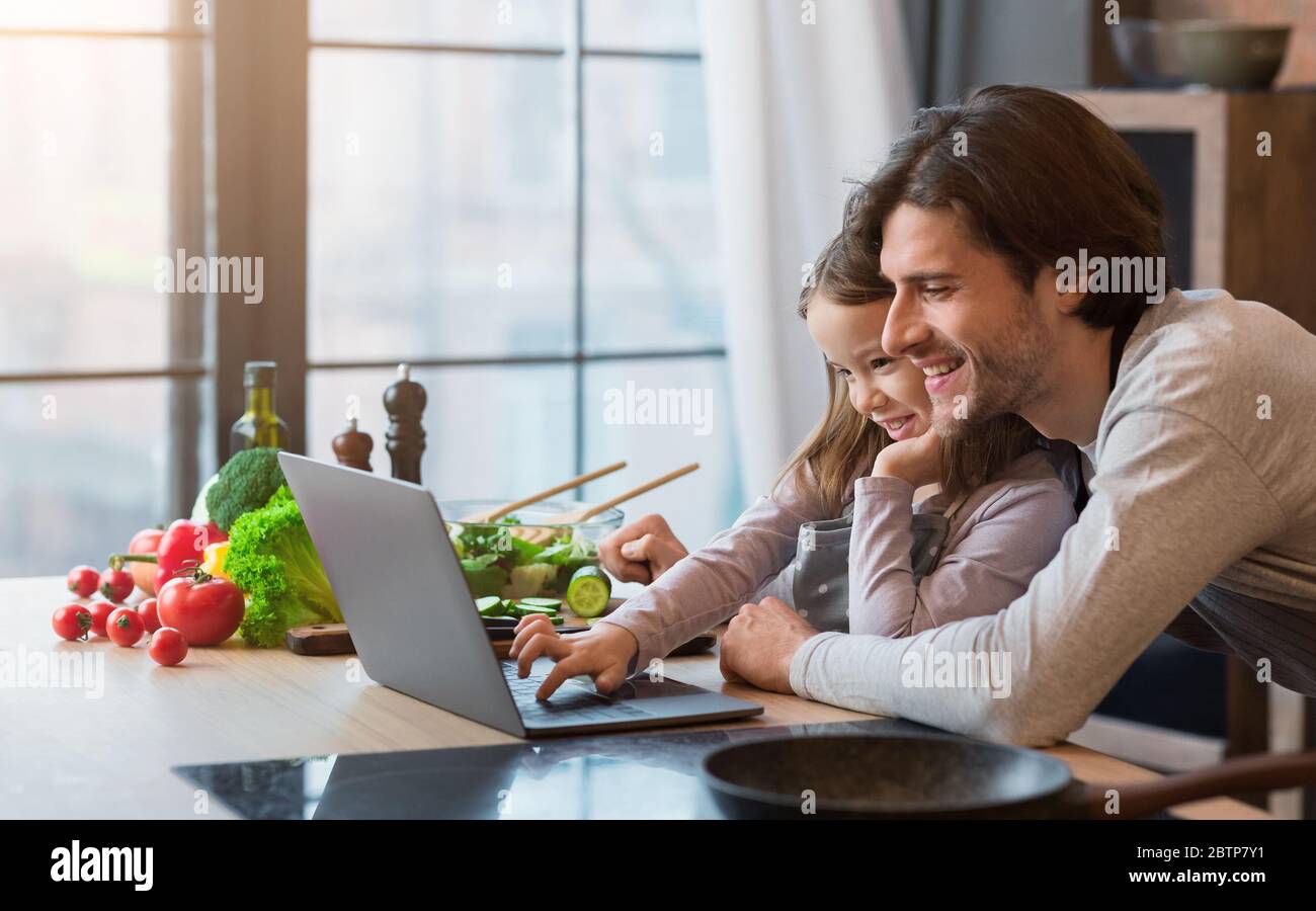 Kulinarischer Blog. Fröhliches Kleines Mädchen Und Ihr Vater Mit Laptop In Der Küche Stockfoto