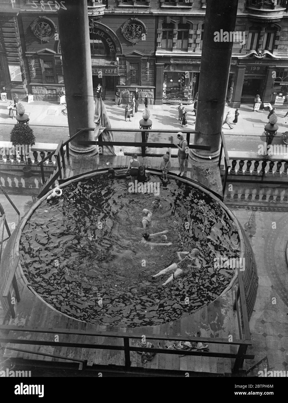 Baden über Piccadilly Verkehr. Auf dem terrassenbeeten Balkon des Piccadilly Hotels wurde ein Pool aufgestellt und die Badegäste tauchen direkt über dem Straßenverkehr ins Wasser. Badegäste im Pool über der Straße. August 1932 Stockfoto