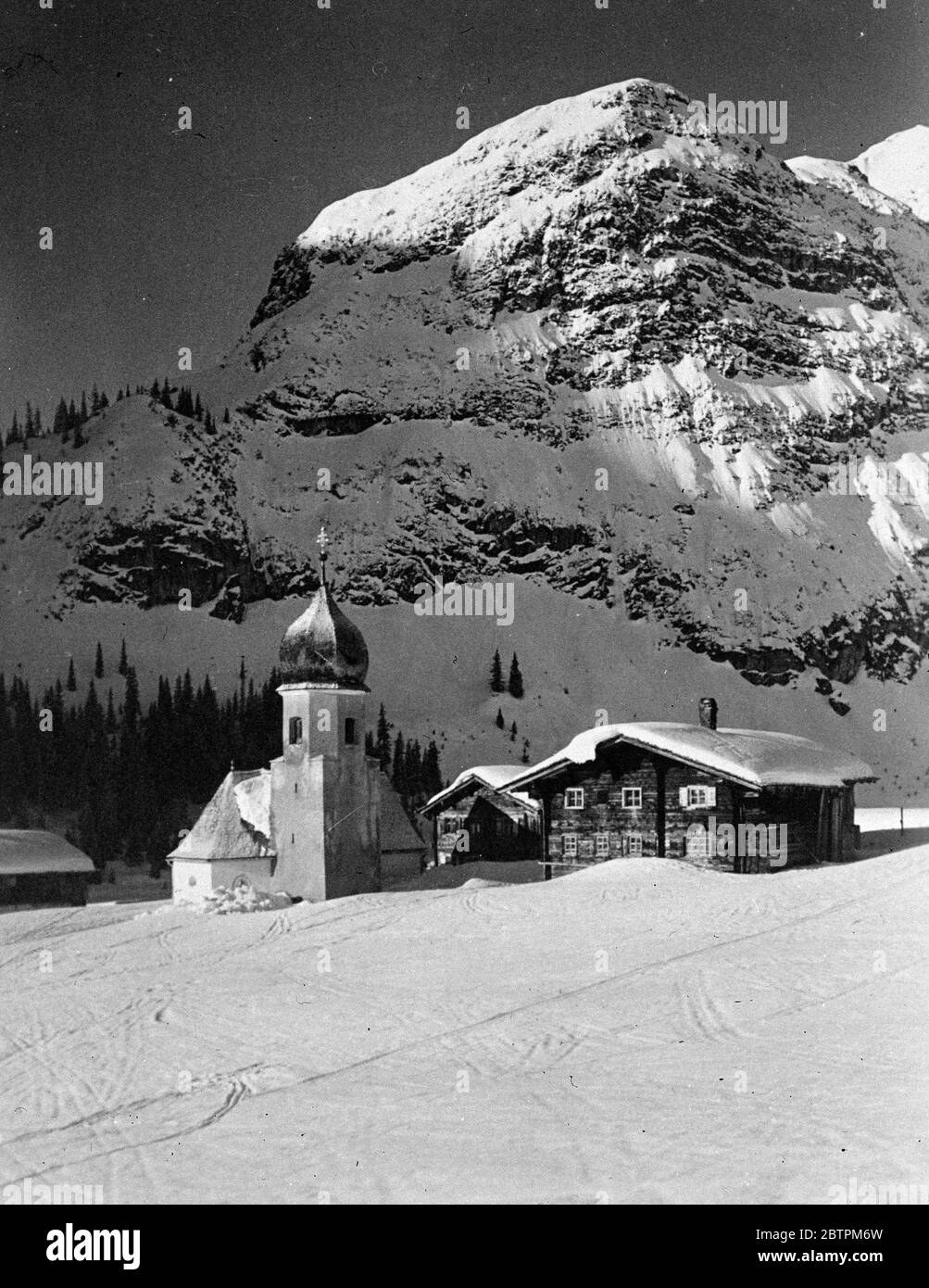 Winter in Tirol . Eine beeindruckende Szene im österreichischen Tirol, als die Strahlen der Wintersonne auf einem schneebedeckten Gipfel hinunterkriechen, an dessen Füßen eine winzige Bergkirche liegt. Dezember 1935 Stockfoto