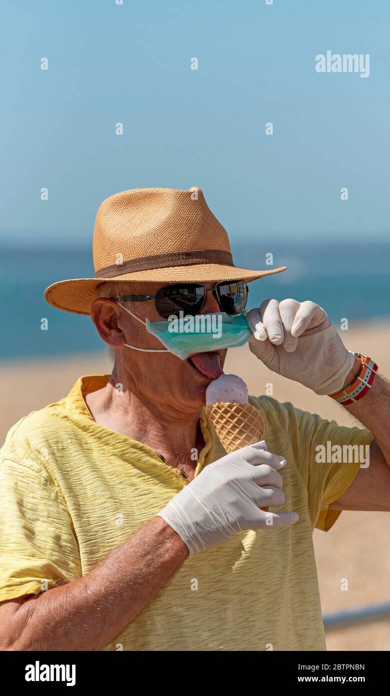 Southsea, Portsmouth, Südengland, Großbritannien. Mai 2020. Mann, der während des Corvid-19 draußen Eis isst, während er eine Maske und Gummischutzhandschuhe trägt Stockfoto