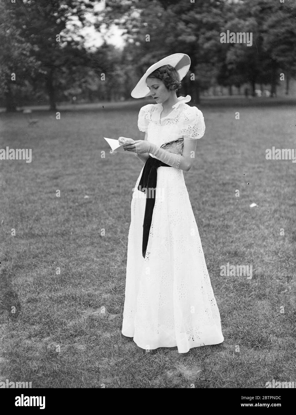 Neue Mode für Ascot. Eine der reizenden Mode, die Ulick Philippe aus London für ascot entworfen hat und nächste Woche eröffnet. Das Kleid ist aus weißem Broderie Anglais locker drapiert mit einem roten Samt Schärpe. Der breite, breite Strohhut ist passend mit rotem Samt verziert. Juni 1937 Stockfoto