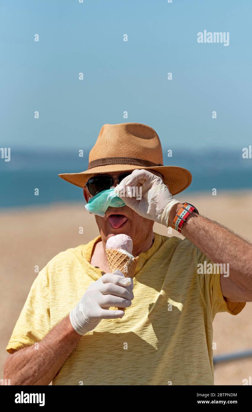 Southsea, Portsmouth, Südengland, Großbritannien. Mai 2020. Mann, der während des Corvid-19 draußen Eis isst, während er eine Maske und Gummischutzhandschuhe trägt Stockfoto