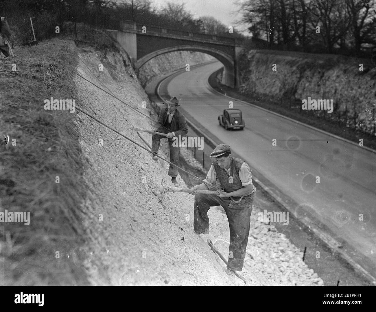 Auf den Surrey Alpen! Arbeiter, mit Sicherheitsseilen um ihre Taille gewickelt, Entfernen bröckelnden Kreide, aber ist eine Gefahr für Autofahrer, auf dem hohen Damm. An der Umgehungsstraße von Guildford, Surrey. 27. Januar 1938 Stockfoto