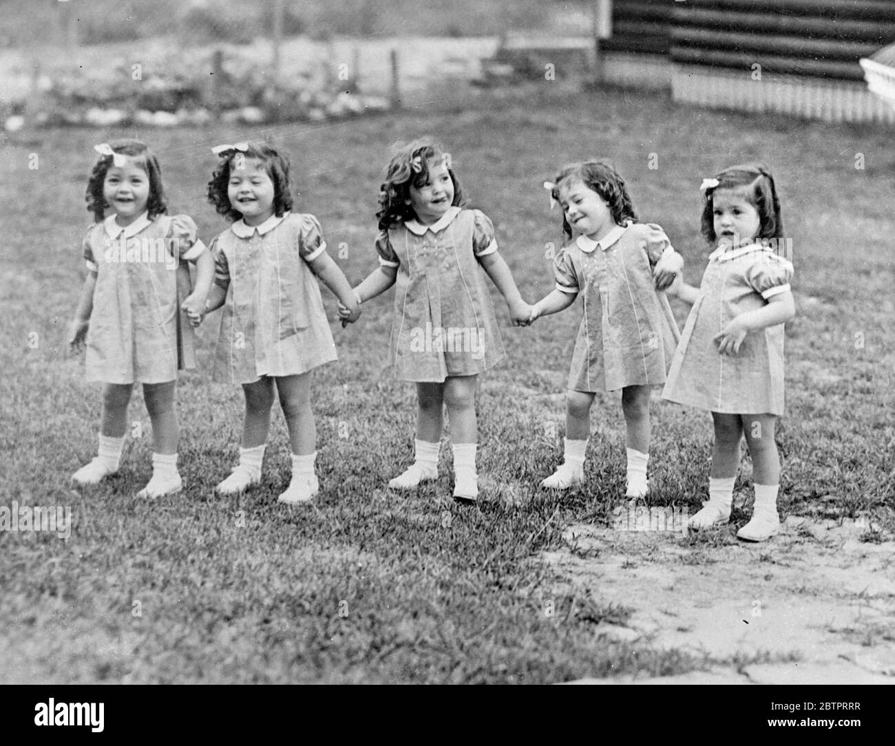 Die Sänften spielen. Hand in Hand die lockigen, robusten Dionne Quintuplets bilden sich in freudiger Erwartung eines Tops auf dem Gelände der Kinderstube in Callander, Ontario. Von links nach rechts, Cecile, Annette, Yvonne, Marie und Emilie. November 1937 Stockfoto