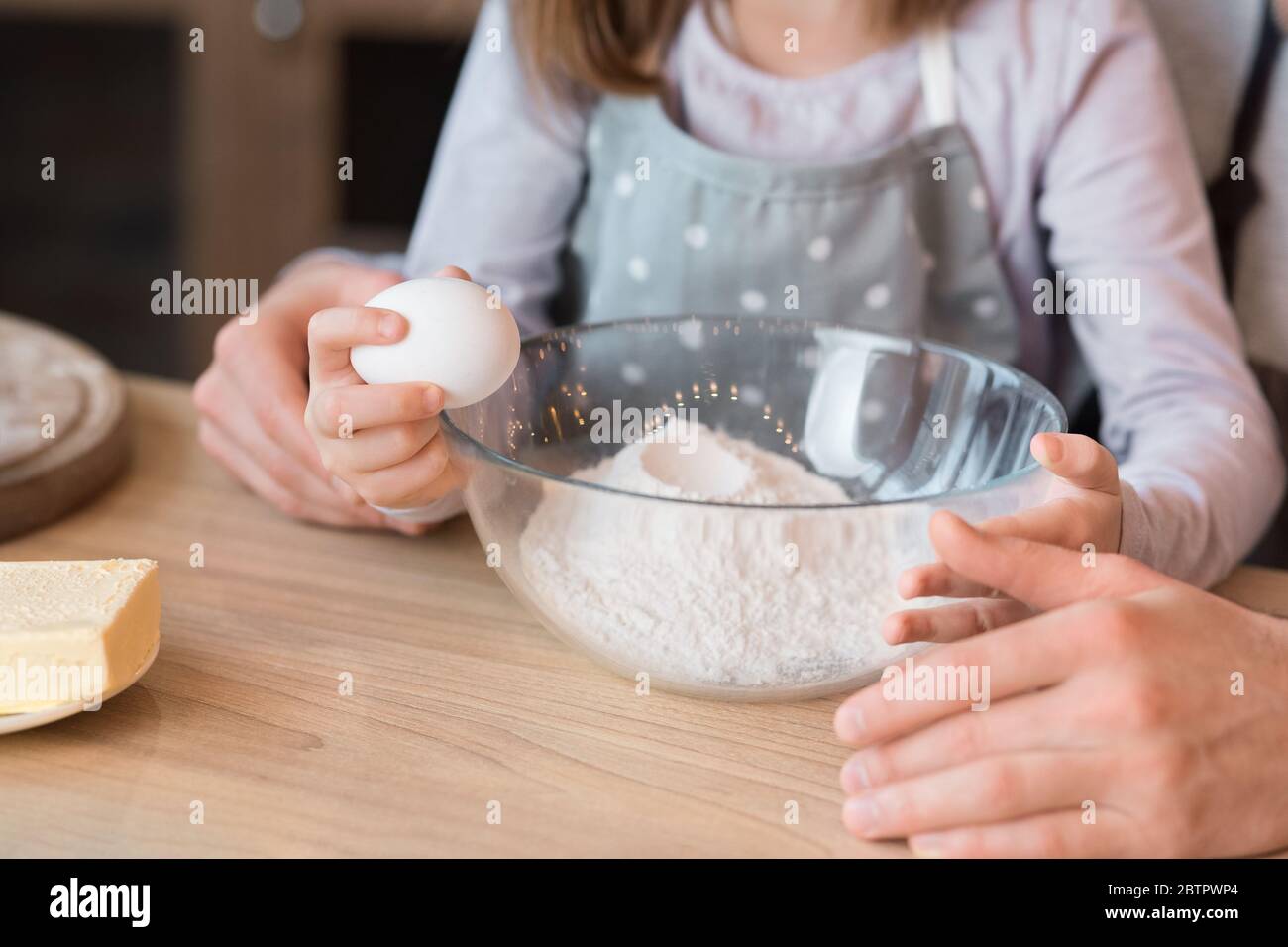 Kleines Mädchen knackt Ei in Schüssel, hilft Vater mit dem Kochen Gebäck Stockfoto
