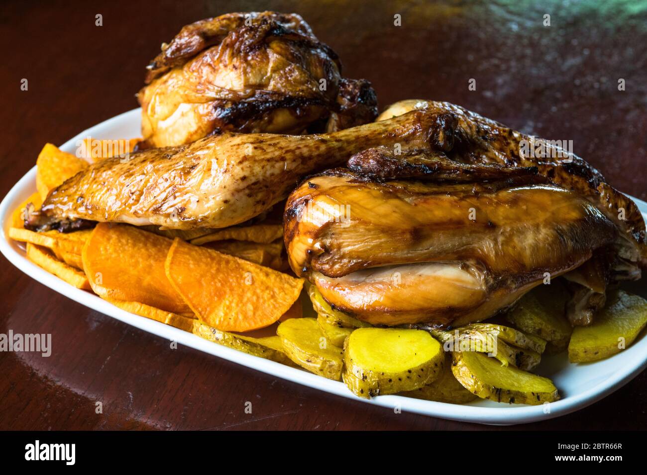 Gebratene Hähnchenfilets, garniert mit Kartoffeln und Süßkartoffeln. Selektiver Fokus. Peruanisches gegrilltes Huhn Stockfoto