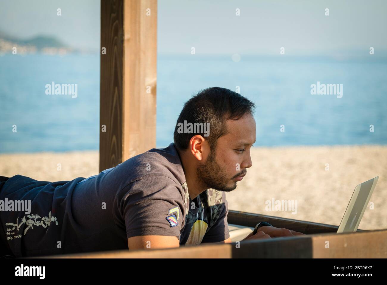 Ein Mann, der am Strand einen Laptop benutzt Stockfoto