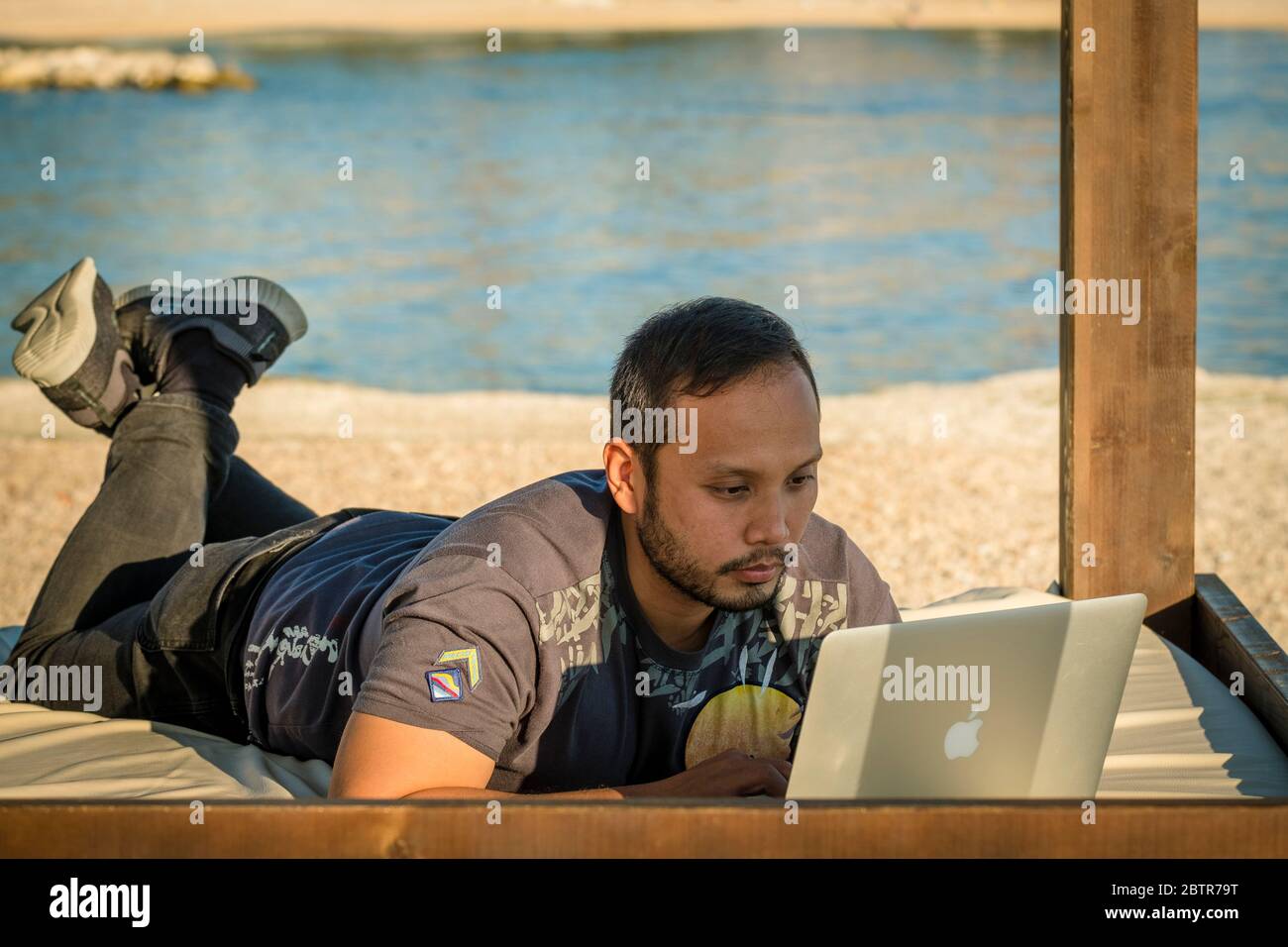 Ein Mann, der am Strand einen Laptop benutzt Stockfoto