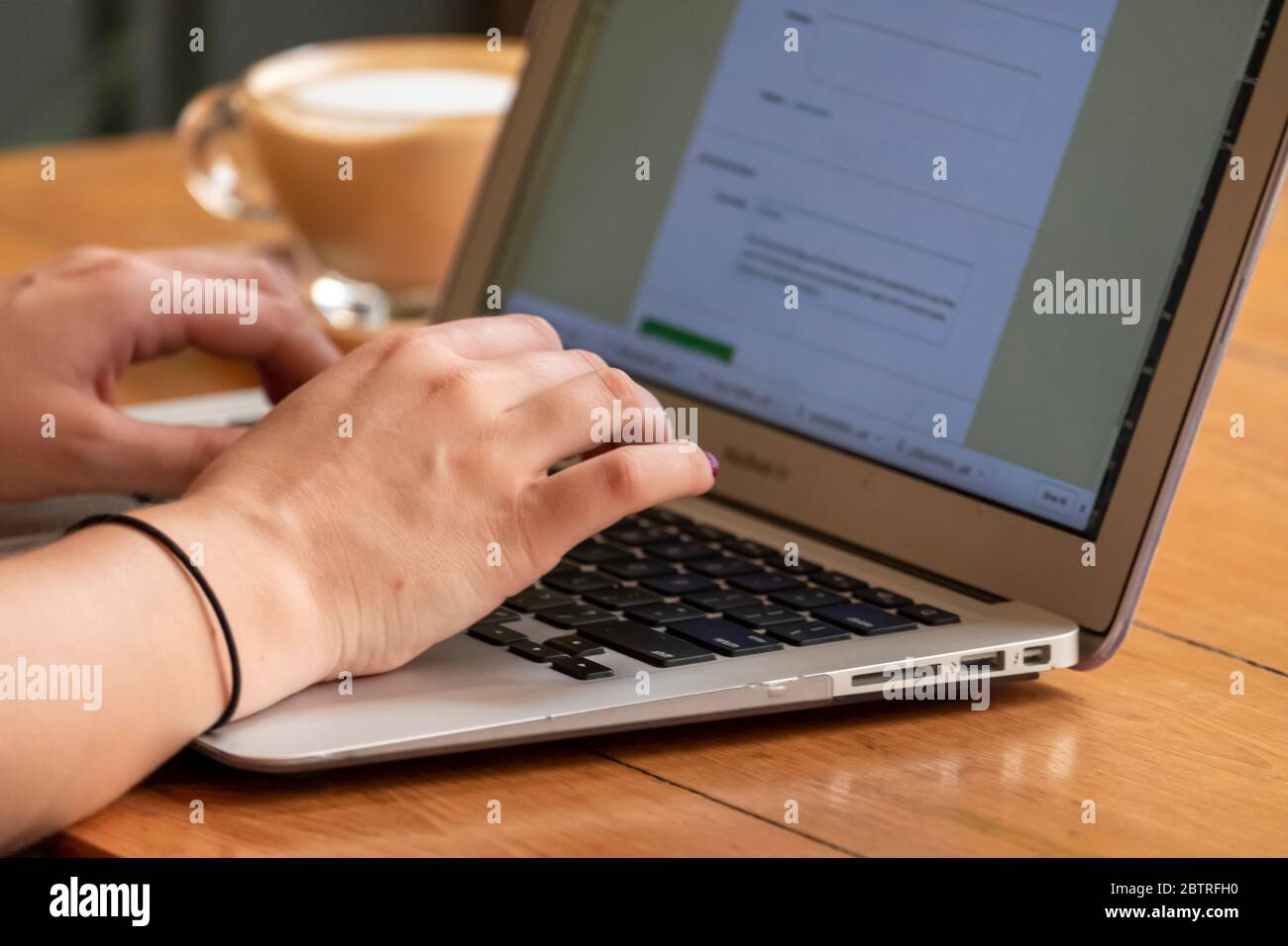 Eine Frau, die an einem Laptop arbeitet, mit einer Tasse Kaffee in einem Home Office oder Café Stockfoto
