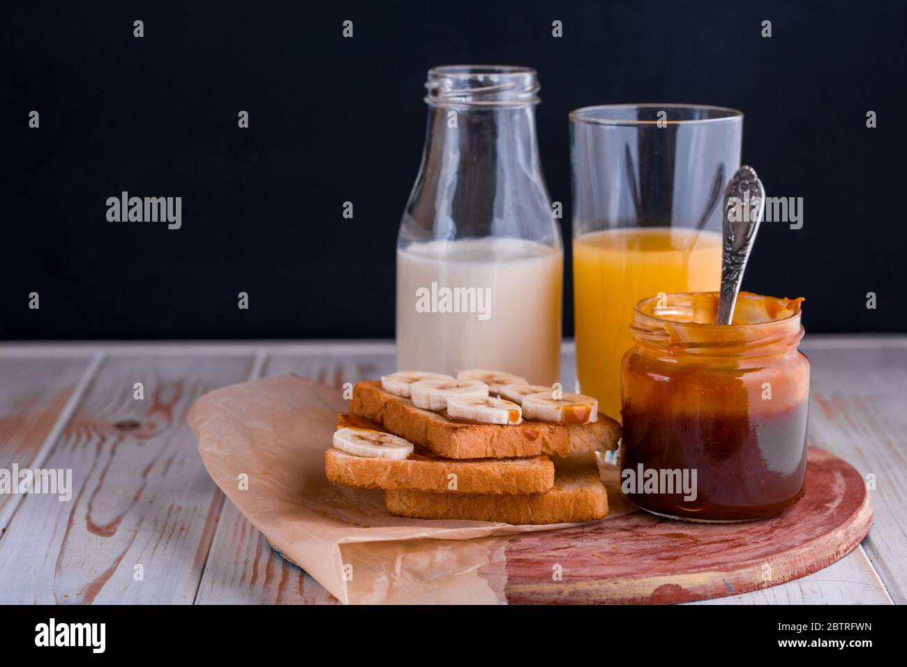 Zwei leckere Toasts mit gesalzenem Karamell und Bananen auf dem Tisch. Ein gesundes Frühstück mit Milch. Stockfoto