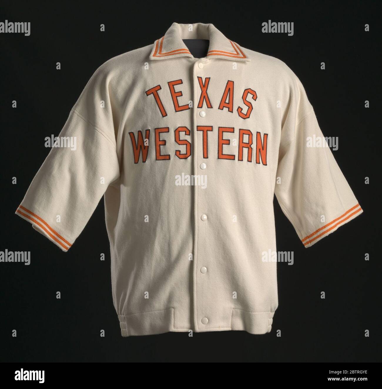 Warm-up Jacke von Jerry Armstrong für Texas Western getragen. Eine weiße Basketball-Trainingsjacke mit orangefarbenen Details, die Jerry Armstrong für das Texas Western College Miners Basketballteam getragen hat. Die Jacke hat kurze Ärmel und befestigt die Mitte vorne mit Metallknöpfen. Stockfoto