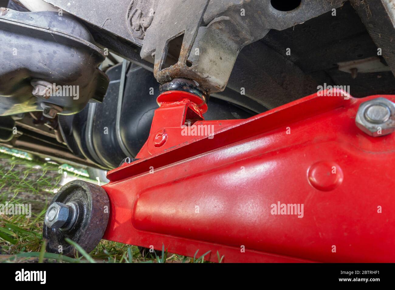 POV-Aufnahme eines schweren hydraulischen Wagenhebers/Wagenhebers auf dem Boden unter einem Van, verbunden mit einem Hebepunkt, mit dem Fahrzeug angehoben. Stockfoto