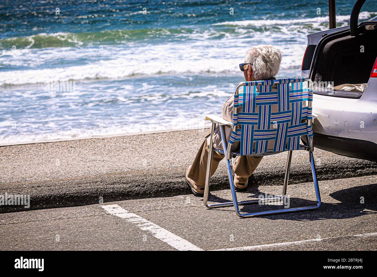 Ein Herr sitzt ganz allein auf einem Parkplatz, der aussieht wie die neue Safe Space Linie jeder muss hinter sich bleiben, jetzt, da die Strände offen sind. Stockfoto