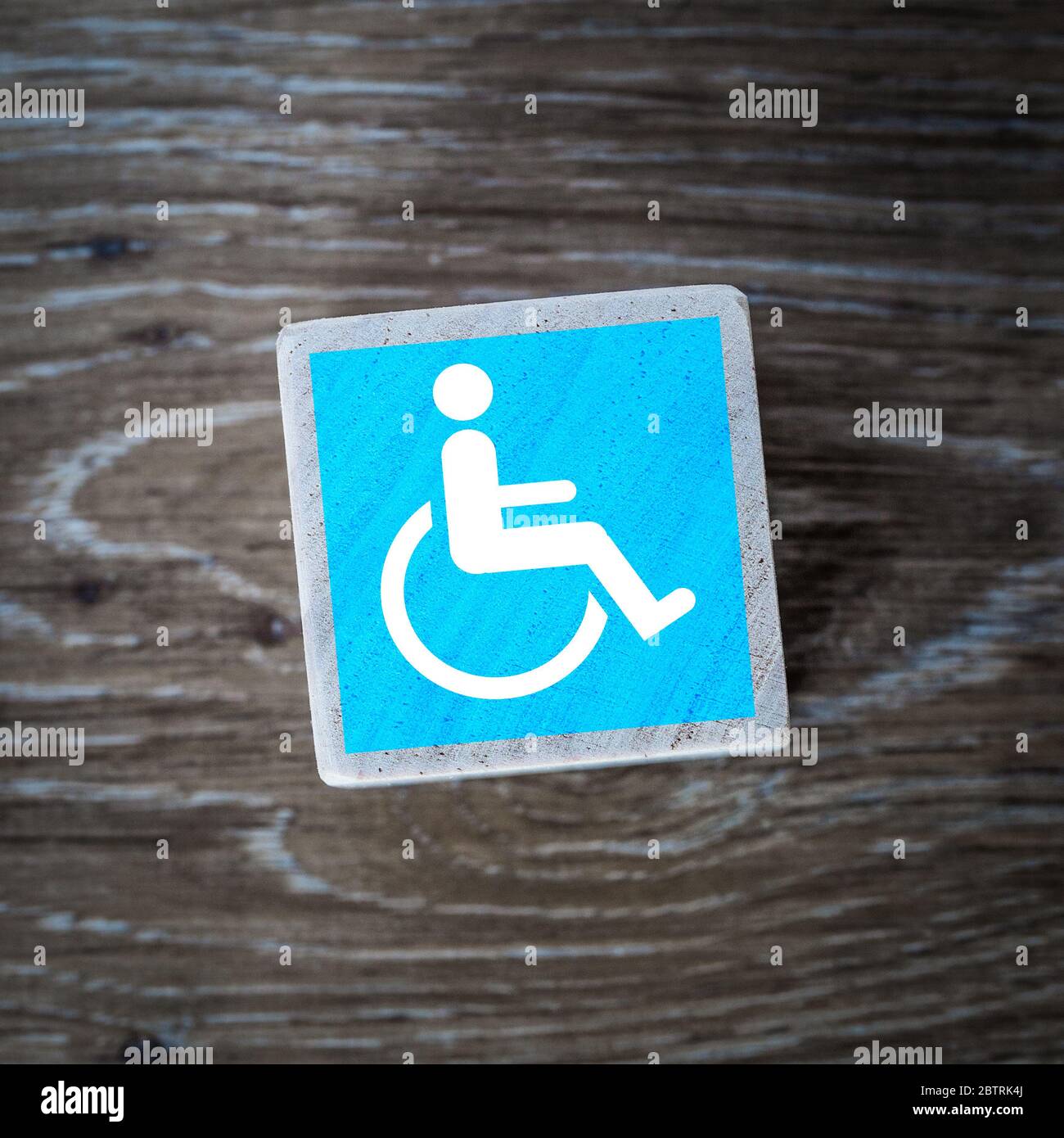 Ein blaues Behindertenzeichen, Symbol oder Symbol für geistig behinderte und körperlich behinderte Menschen auf einem Holzblock mit Holzhintergrund und Kopierfläche Stockfoto
