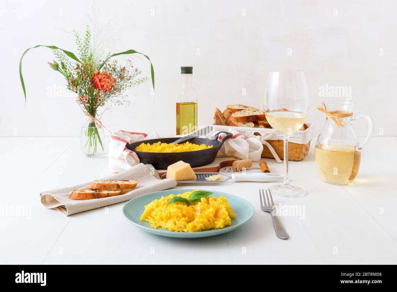 Risotto Mailänder, Holztisch mit traditionellem italienischen Safranrisotto, Gläsern und Krug Wein, Flasche Olivenöl, Korb mit Brot und Blumen Stockfoto