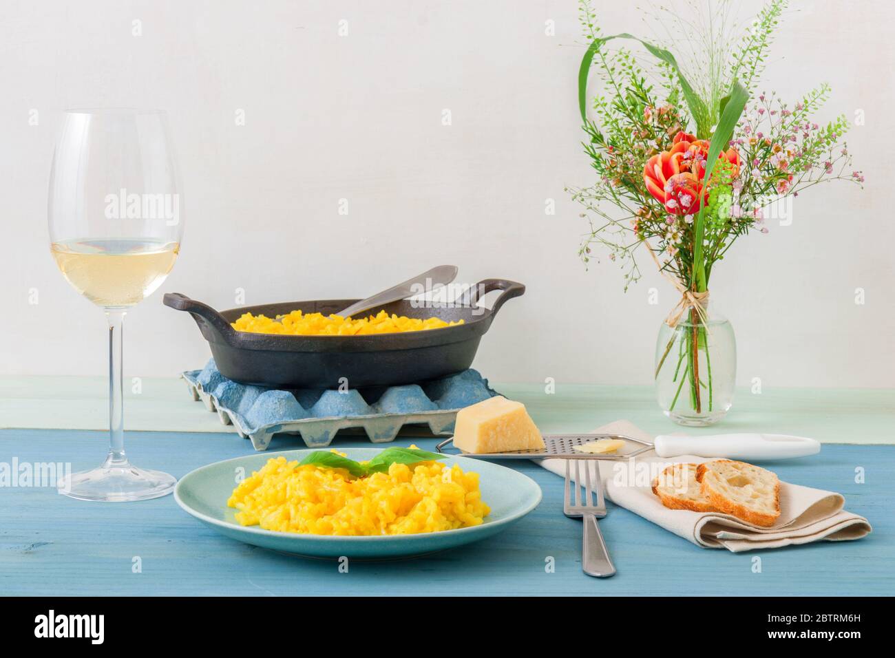 Risotto Mailänder, Holztisch mit traditionellem italienischen Safranrisotto, Gläsern und Krug Wein, Flasche Olivenöl, Korb mit Brot und Blumen Stockfoto