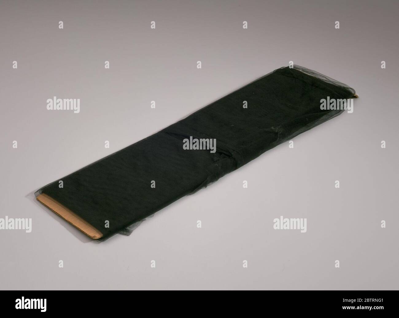 Bolzen aus schwarzem Tüllstoff von Maes Millinery Shop. Schwarzer synthetischer Tüll umwickelt ein Stück Pappe. Ein Herstelleretikett wird an einem Ende der Pappe mit durchgestrichenen Druckschriften aufgeklebt. Stockfoto