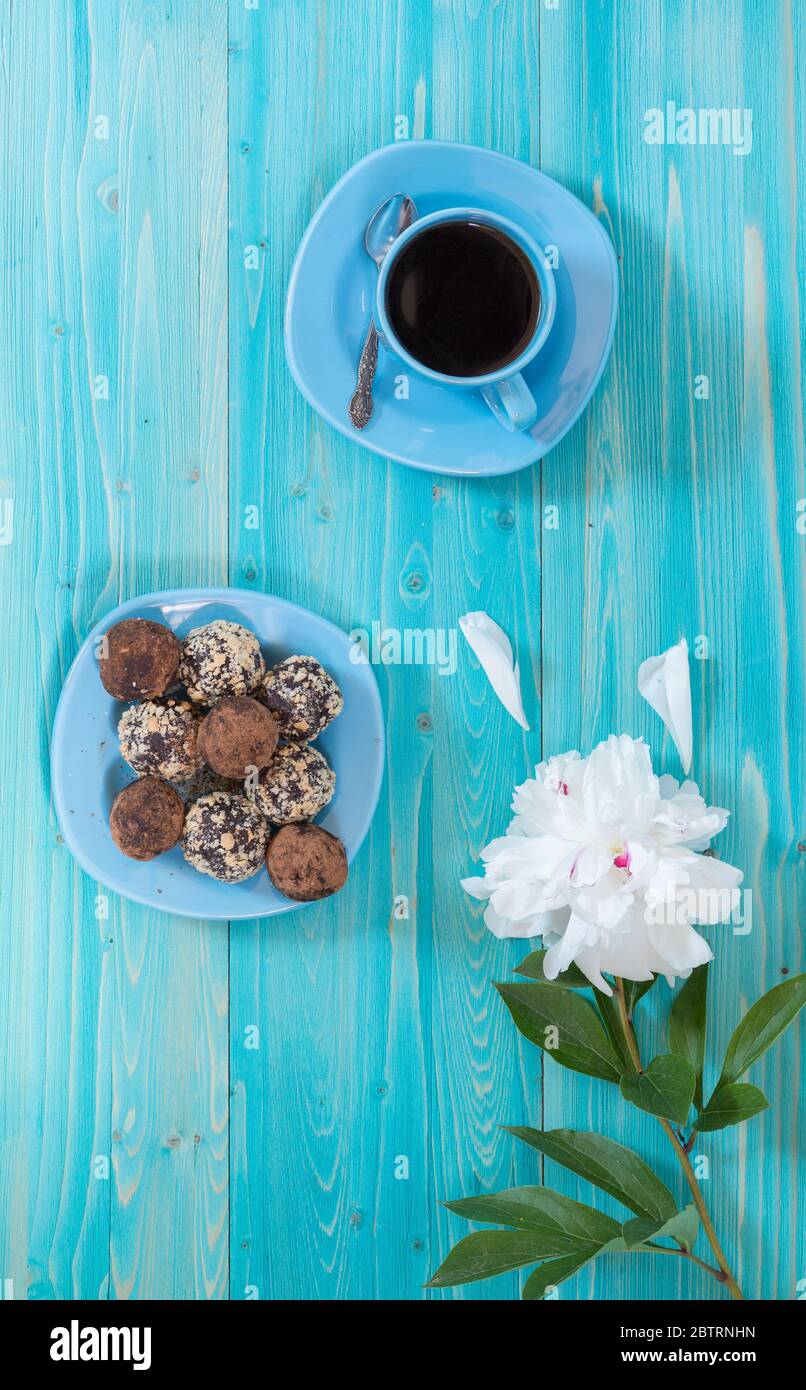 Eine Tasse Kaffee, eine weiße Pfingstrose und Energiekugeln auf einem Teller. Gesunde hausgemachte Schokolade Dessert zum Frühstück wird Sie mit Energie zu füllen. Sprotte Stockfoto