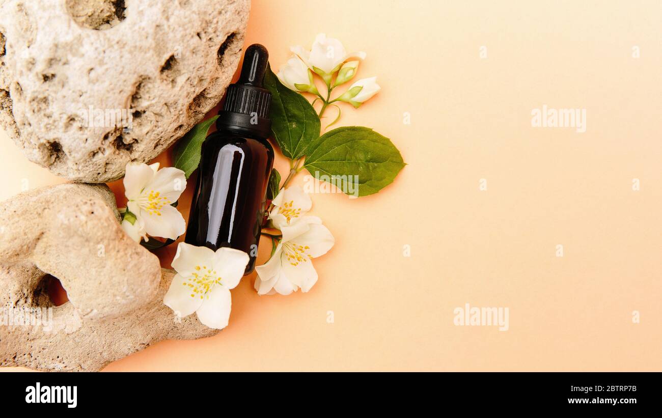 Schöne Komposition mit Teöl. Glas Kosmetikflaschen stehen auf einem Stein mit Jasmin auf einem beigen Hintergrund mit hellem Sonnenlicht. Naturkosmetik Konzept, natürliches ätherisches Öl Stockfoto