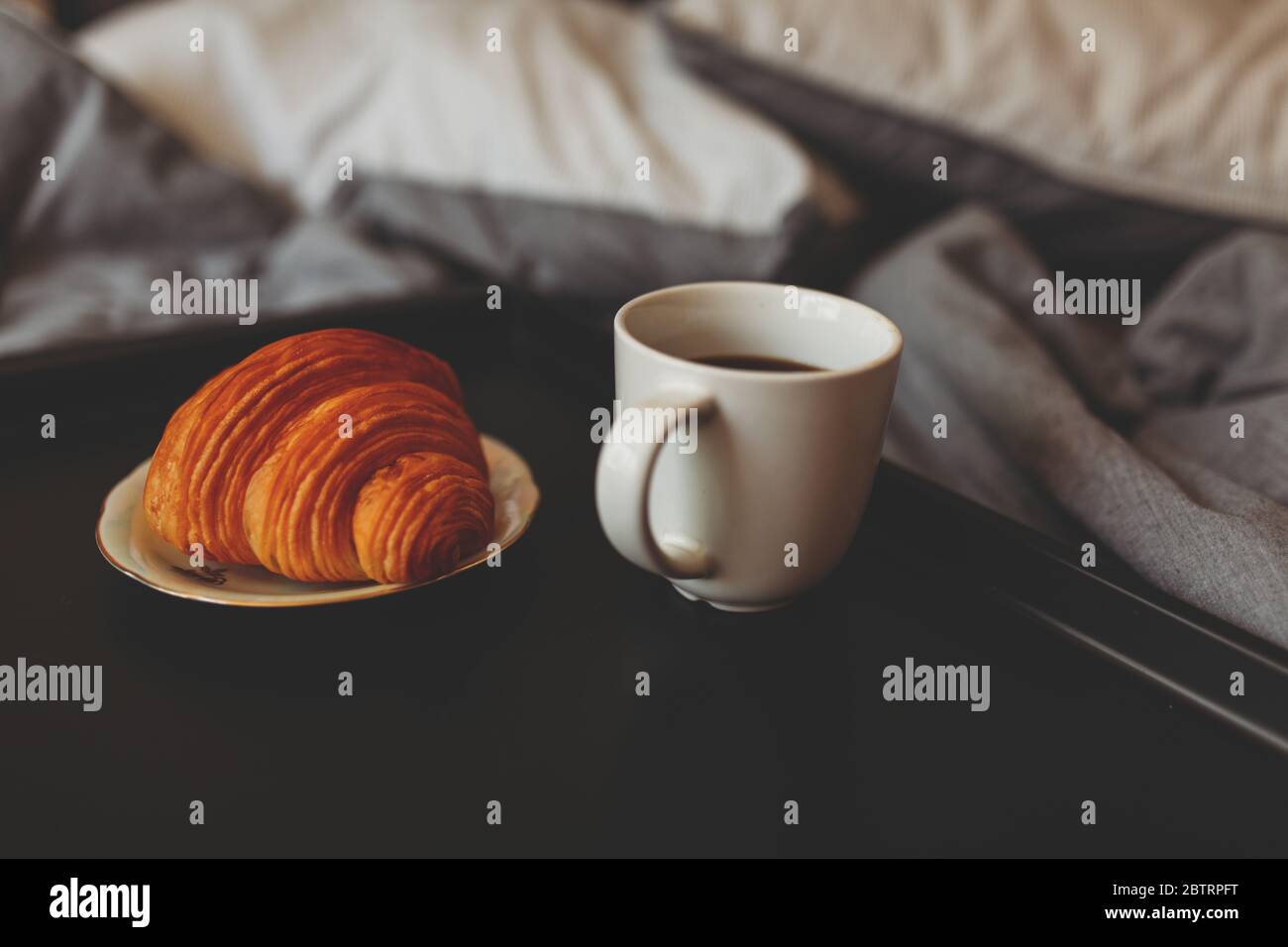 Frühstück auf einem Tablett im Bett zu Hause weiße dunkle Bettwäsche. Croissant Tee Erdbeeren. Stockfoto