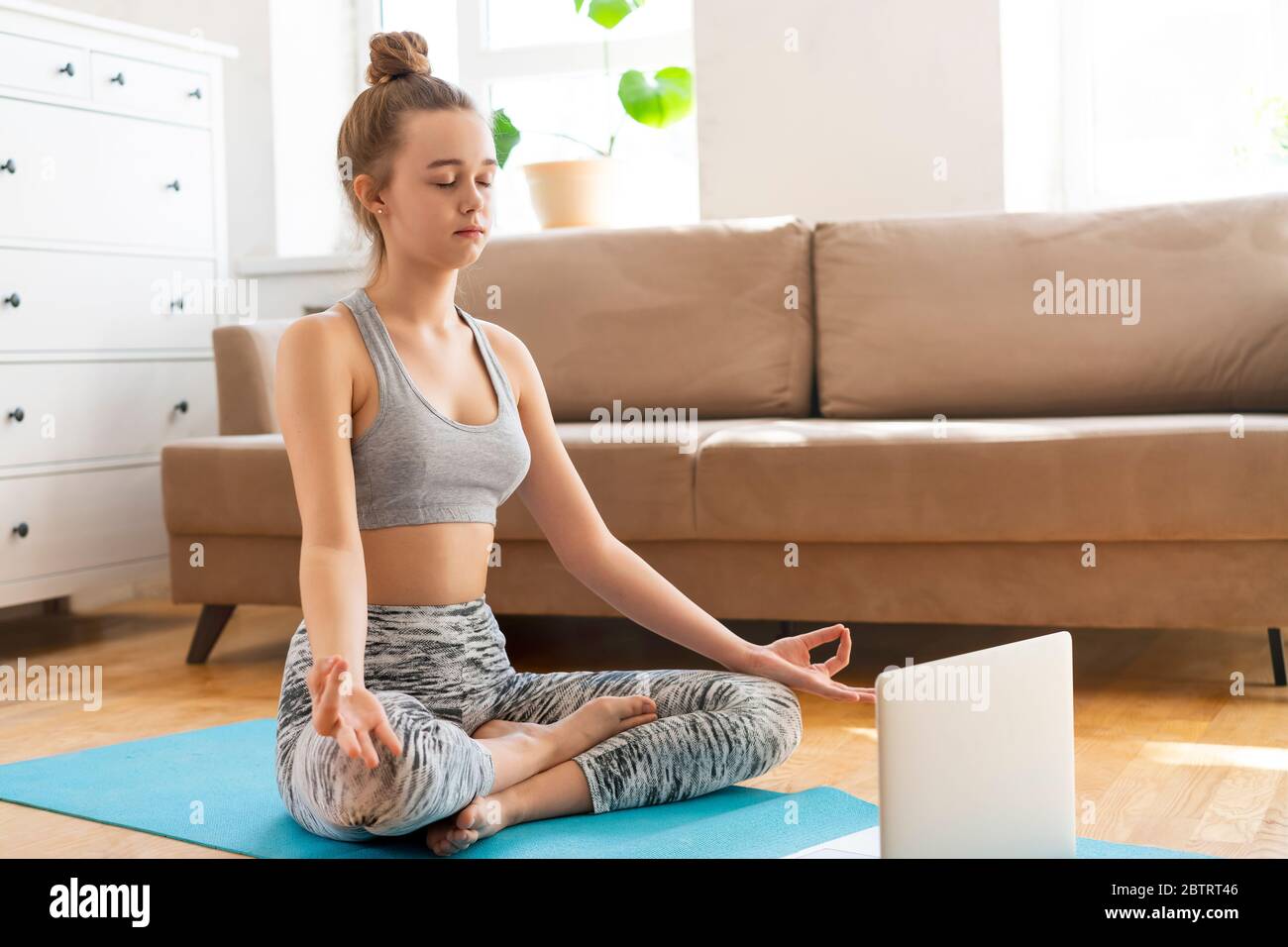 Junge attraktive Frauen tun Yoga-Übung zu Hause Yoga zu Hause in der Lotusposition, Ardha Padmasana Übung, halb Lotus Pose im Wohnzimmer. Sport mit BH und Hose. Gesundheitskonzept Stockfoto