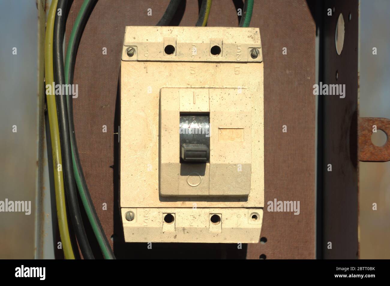 Ein alter elektrischer Schalter aus Kunststoff ist weiß in einem eisernen Kasten mit Drähten. Stockfoto