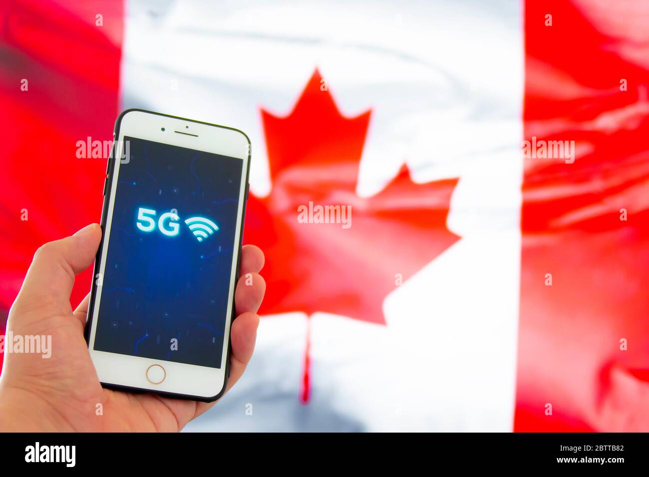 Calgary, Alberta, Kanada. 27.Mai 2020. Eine Person, die ein iPhone mit einem 5G-Zeichen auf einem Hintergrund mit einer nicht fokussieren kanadischen Flagge hält Stockfoto