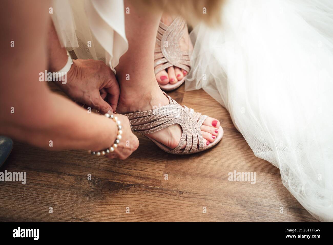 Brautjungfer hilft Braut, Schuhe anzuziehen. Nahaufnahme der Hände, die stilvolle Schuhe auf dem Fuß der Braut tragen. Konzept für Hochzeitstag. Stockfoto