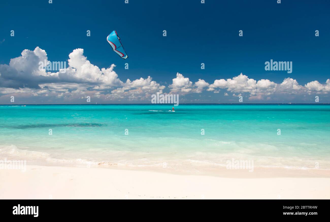 Kitesurfer mit Kiteboard vor einem atemberaubenden und menschenleeren tropischen Strand, am Horizont der blaue Himmel und weiße Wolken Stockfoto