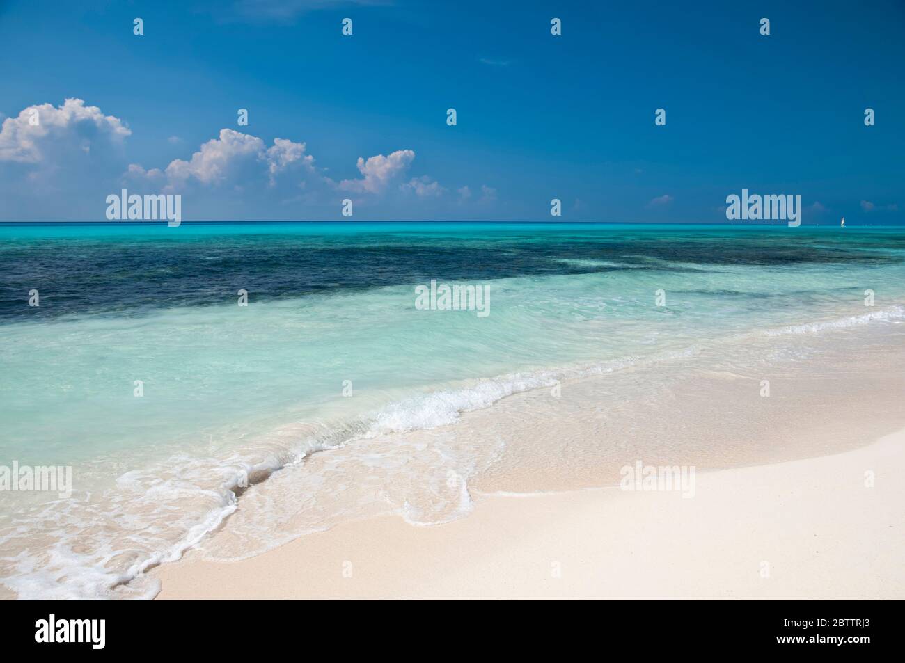 Menschenleerer und paradiesischer karibischer Strand, mit einem ruhigen und türkisfarbenen Meer, mit einem Segelboot, das bis zum Horizont segelt Stockfoto
