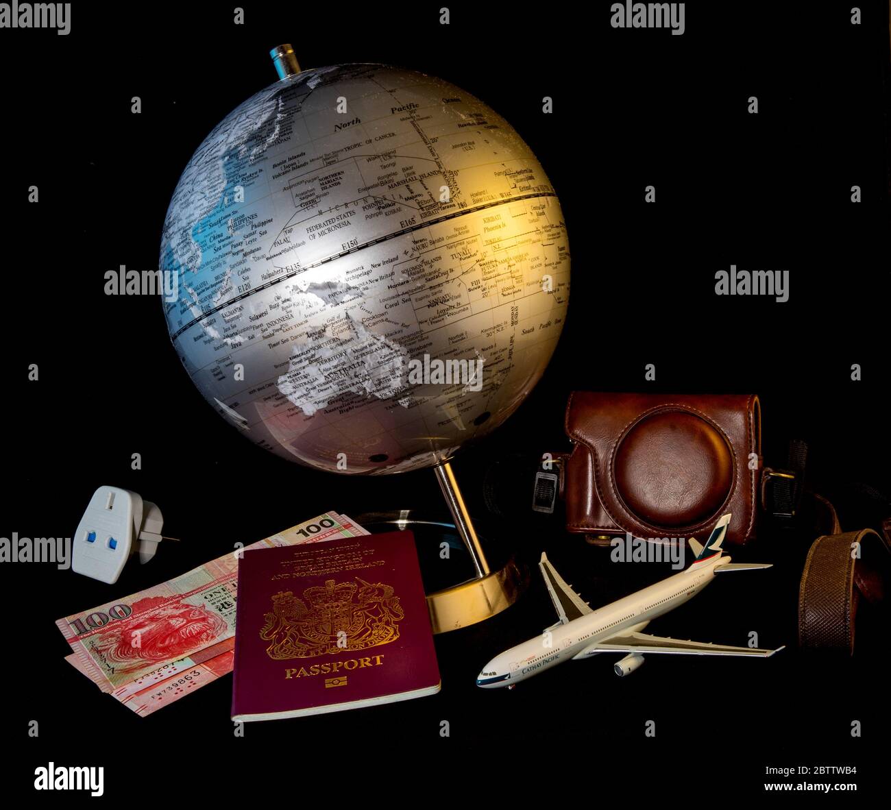 Auswahl von reisebezogenen Gegenständen rund um einen Planeten. Die Artikel umfassen einen Reisepass, Reisegeld, Modellflugzeug, Kamera und Reisesteckadapter. Stockfoto
