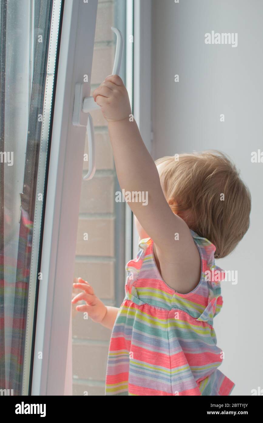 Kleines Mädchen öffnet das Fenster. Sicherheit für Kinder zu Hause. Vermeidung von Sturzunfällen Stockfoto