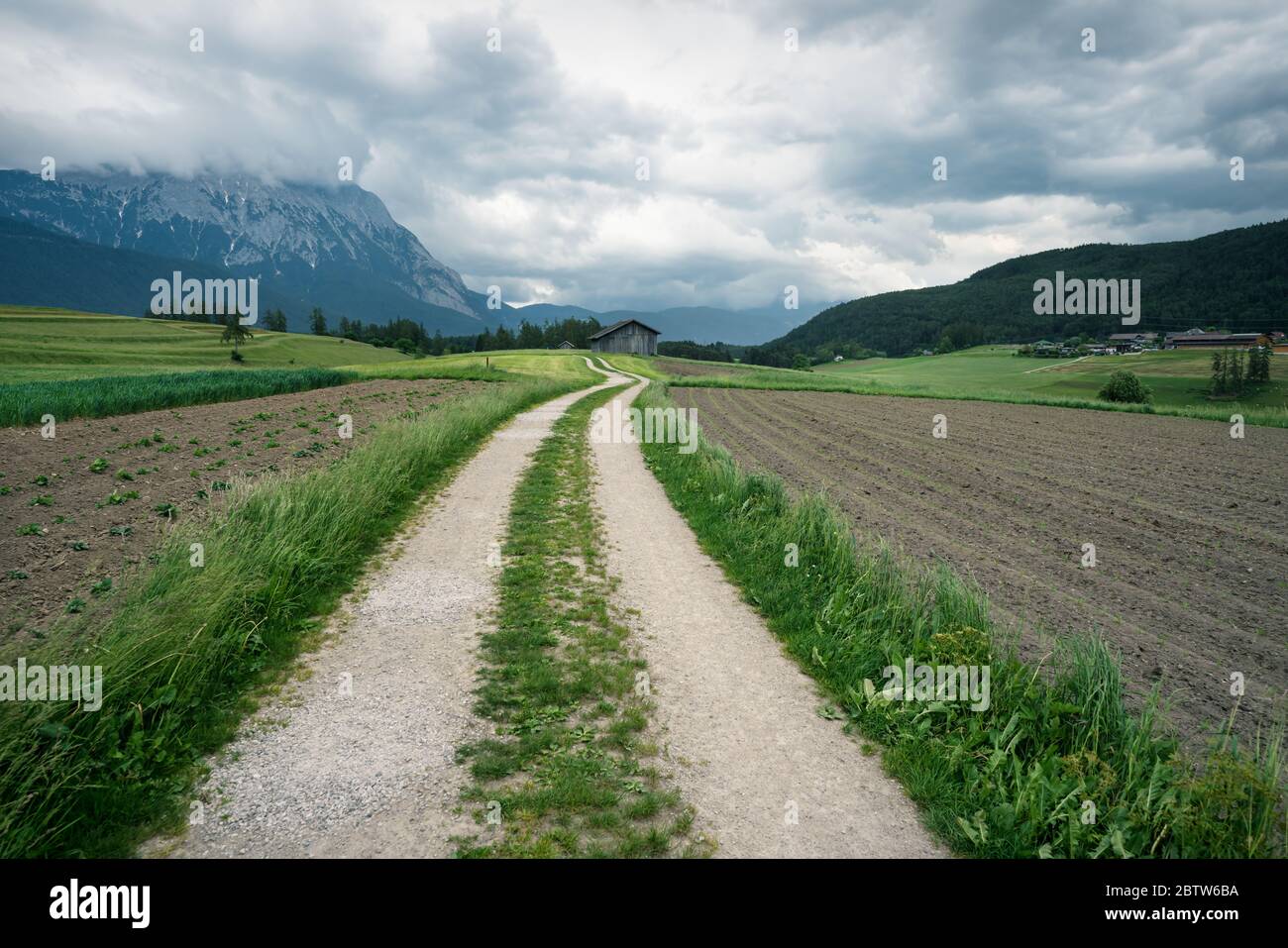 Kurvenreicher Pfad durch Ackerland mit österreichischen Alpen und stürmischem Wetter, Mieminger Plateau, Tirol, Österreich Stockfoto