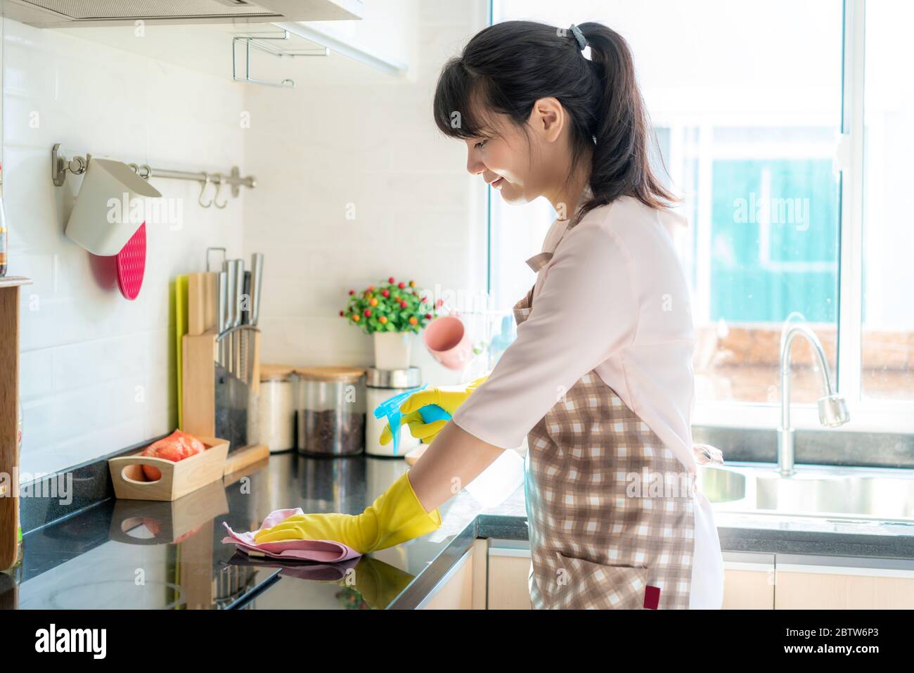 Asiatische Frau trägt Gummi Schutzhandschuhe Reinigung Küchenschränke in ihrem Haus während des Aufenthalts zu Hause mit Freizeit über ihre tägliche Haushälterin Stockfoto
