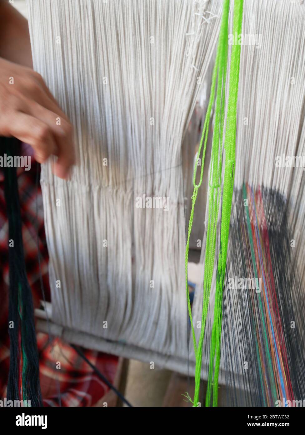 Ansicht der Hände eines Webers, der Baumwollfäden auf einem mechanischen Webstuhl anordnet. Stockfoto