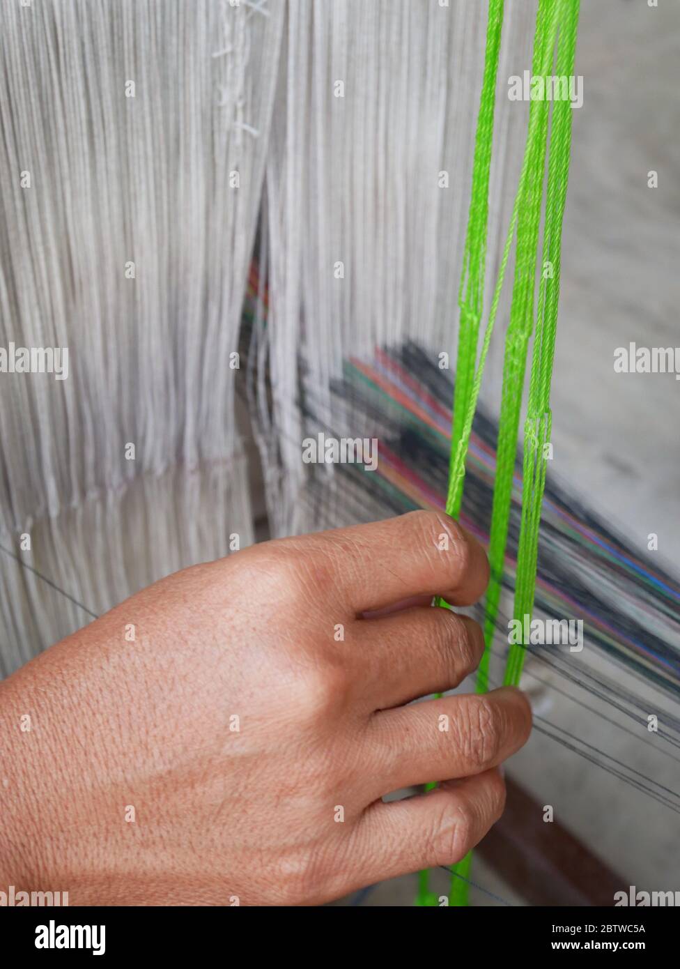 Ansicht der Hände eines Webers, der Baumwollfäden auf einem mechanischen Webstuhl anordnet. Stockfoto