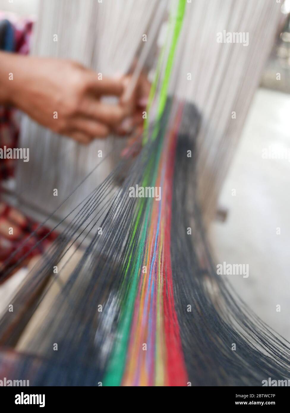 Ansicht der Hände eines Webers, der Baumwollfäden auf einem mechanischen Webstuhl anordnet. Stockfoto