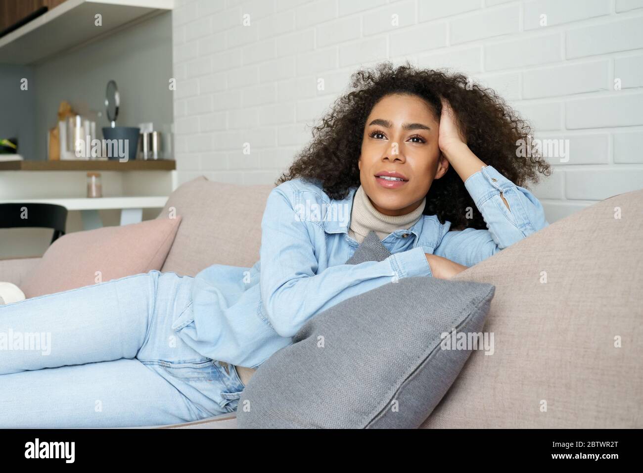 Heitere entspannte afrikanische Frau Lounge auf einem bequemen Sofa, träumen zu Hause. Stockfoto