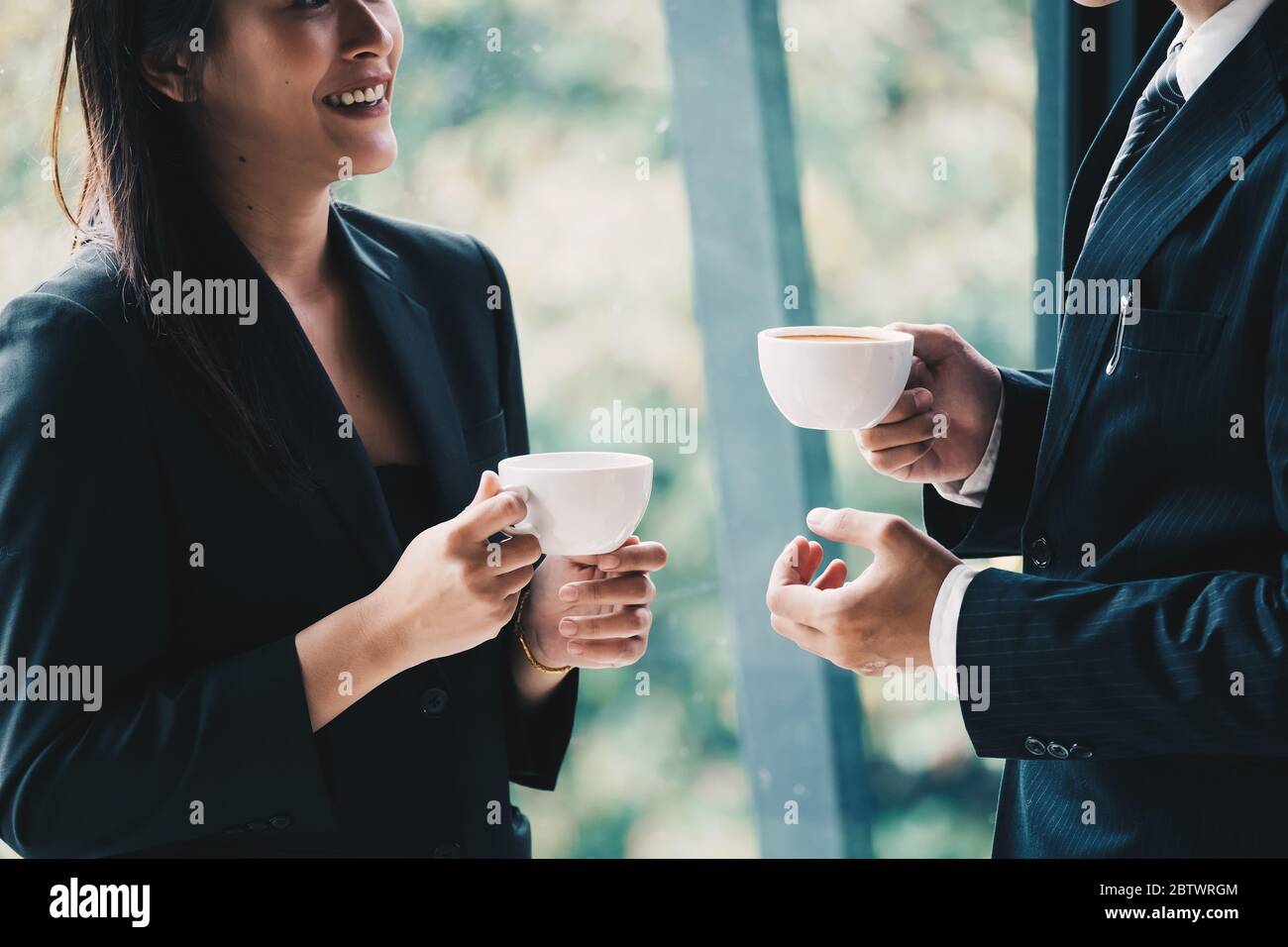 Kaffeepause. Gruppe Geschäftsleute, stehen in modernen Büro, halten eine Tasse, lächelnd stehen am Fenster Stockfoto